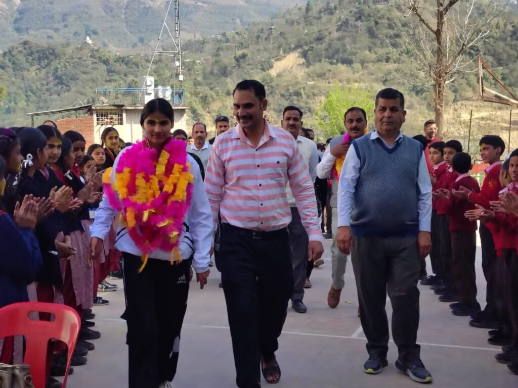 Students and staff of PM Shri Govt Utkrish Sr Sec School, Dharampur, welcome a national-level student athlete with a garland during a felicitation ceremony.
